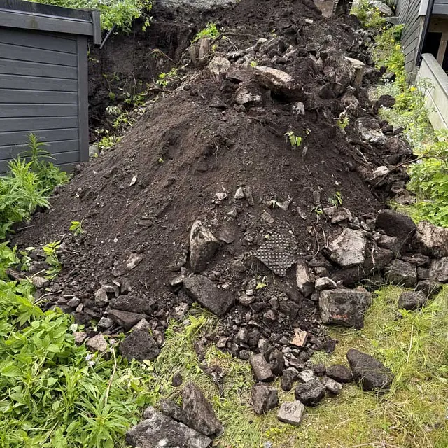 En haug med utgravd jord og stein, med en gravemaskin i bakgrunnen.
