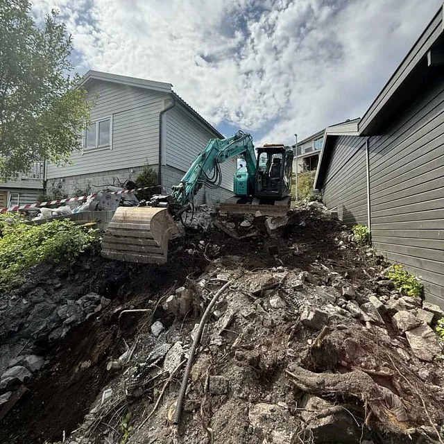 Gravemaskin som arbeider med utgraving av grøft i ulendt terreng etter brudd på pumpeledning.