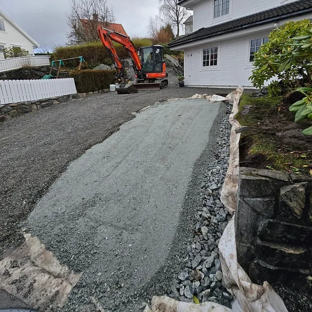 Liten orange gravemaskin utenfor hvit bolighus