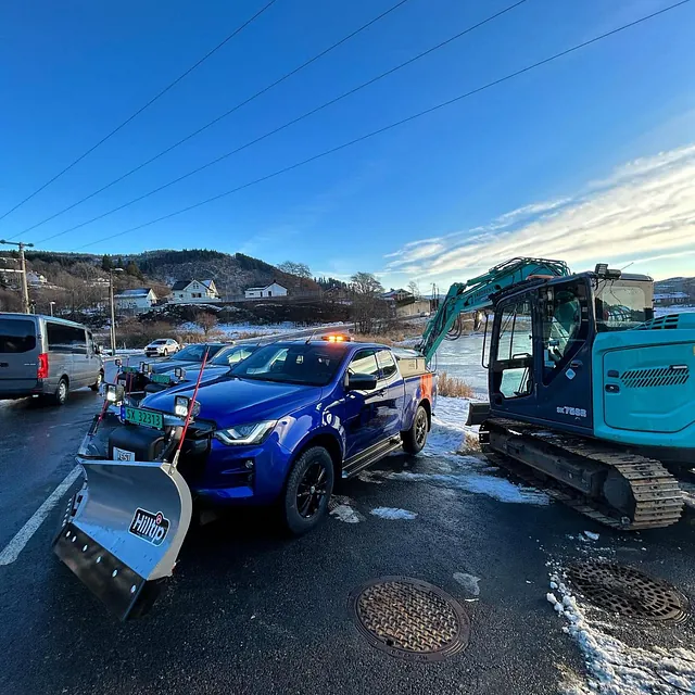 Biler og gravemaskin parkert ved vei