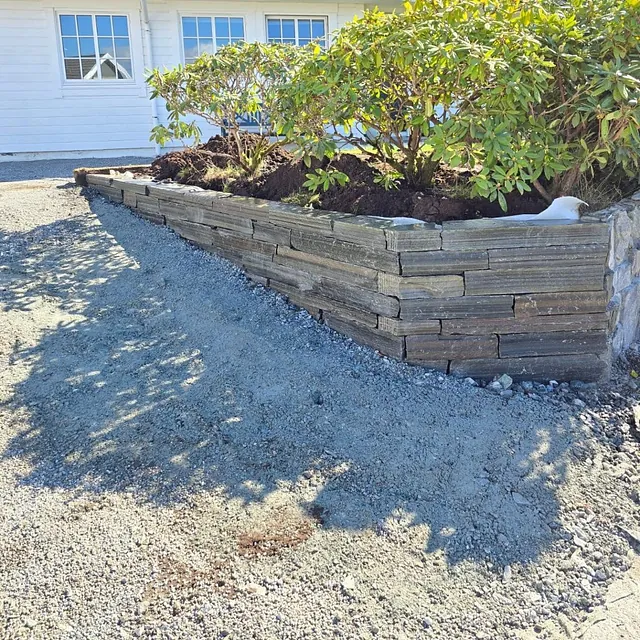 Pent opparbeid innkjøring til hus med mur i stein og busker