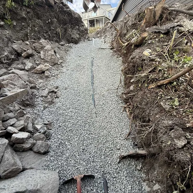 En smal grøft fylt med pukk/grus mellom fjell og terreng.